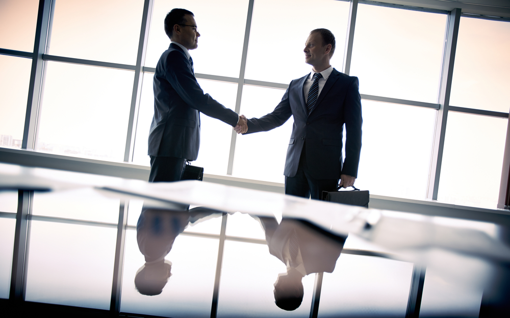 Two men shaking hands over a table.