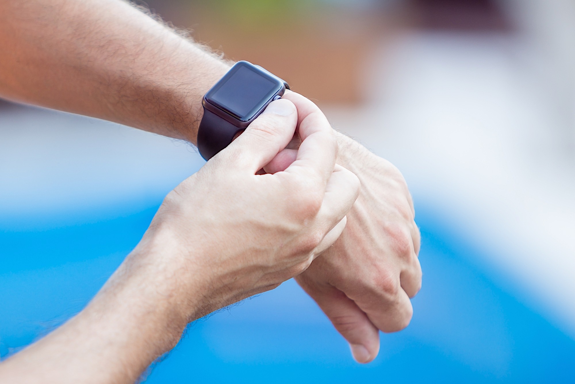 Male hands with black smartwatch on a background of water pool