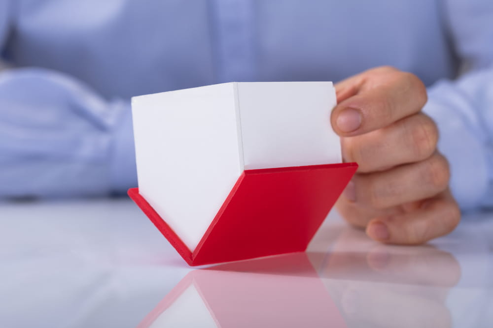 A Fake House Flipped Upside Down on a Table Being Held by a Person's Hand